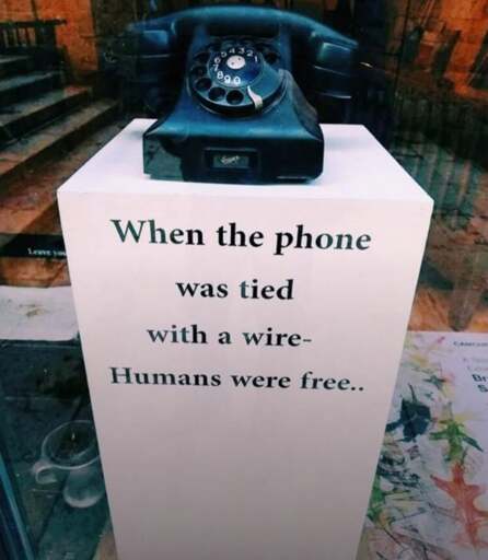Old telephone on a stand that says "When the phone was tied with a wire- Humans were free..."