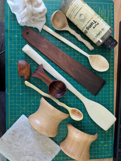 Wooden utensils and objects that have recently been oiled, along with a bottle of pure tung oil, an oily rag, and a superfine scotchbrite pad. 
