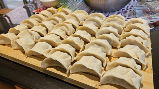 Five rows of six hand made pork dumplings on a wooden cutting board. 