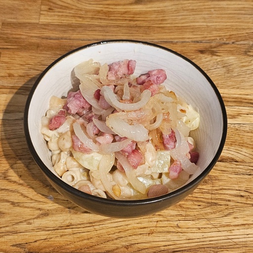 A bowl of Älplermagronen, consisting of creamy pasta and potatoes topped with fried bacon and onion